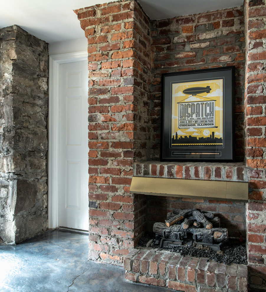 Exemple d'un grand sous-sol chic donnant sur l'extérieur avec sol en béton ciré, une cheminée standard, un manteau de cheminée en brique et un sol gris.