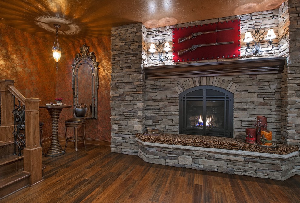 Exempel på en stor klassisk källare utan fönster, med röda väggar, en standard öppen spis, en spiselkrans i sten och mellanmörkt trägolv