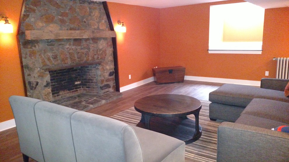 Photo of a medium sized farmhouse look-out basement in Boston with orange walls, dark hardwood flooring, a standard fireplace, a stone fireplace surround and brown floors.