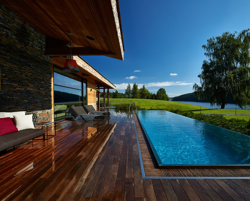 Réalisation d'une piscine à débordement et avant design de taille moyenne et rectangle avec une terrasse en bois.