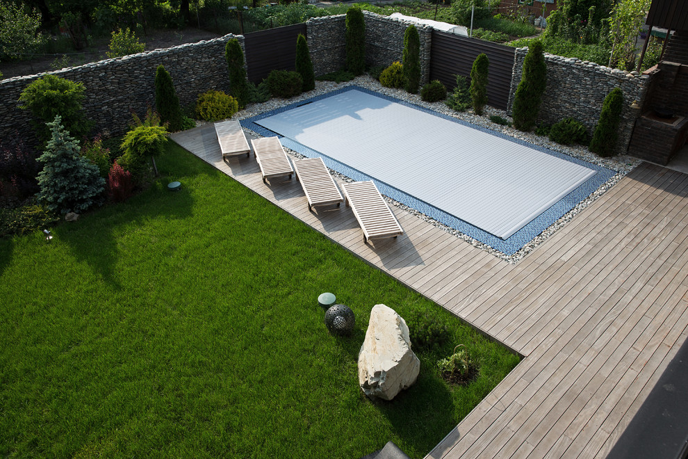 Idée de décoration pour une grande piscine à débordement design rectangle avec une terrasse en bois et une cour.