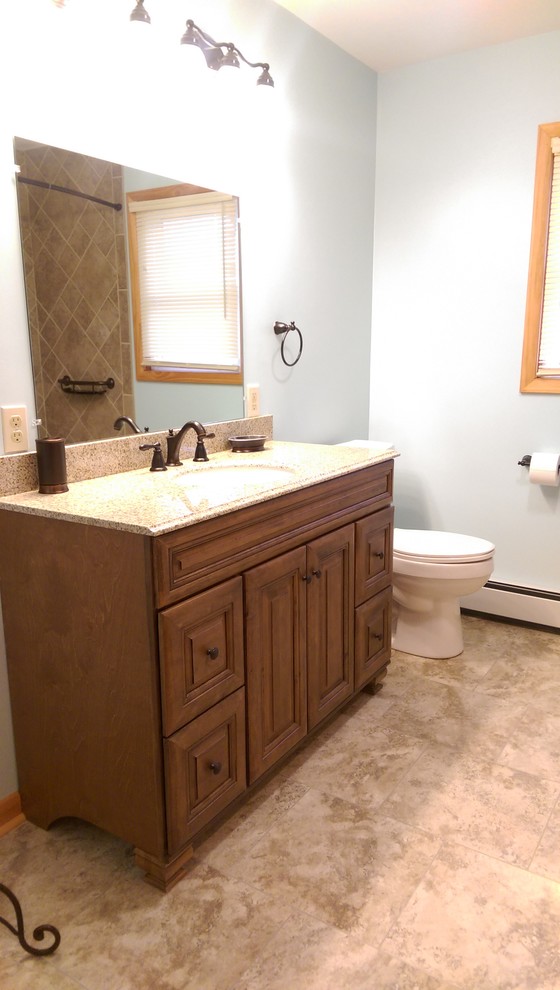 Medium sized classic ensuite bathroom in Other with raised-panel cabinets, dark wood cabinets, an alcove bath, a shower/bath combination, a two-piece toilet, brown tiles, porcelain tiles, blue walls, vinyl flooring, a submerged sink and granite worktops.