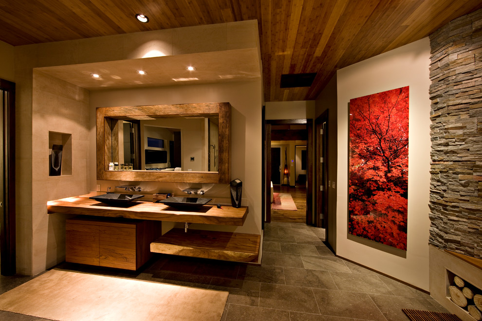 Trendy beige tile bathroom photo in Las Vegas with a vessel sink, flat-panel cabinets, medium tone wood cabinets and wood countertops