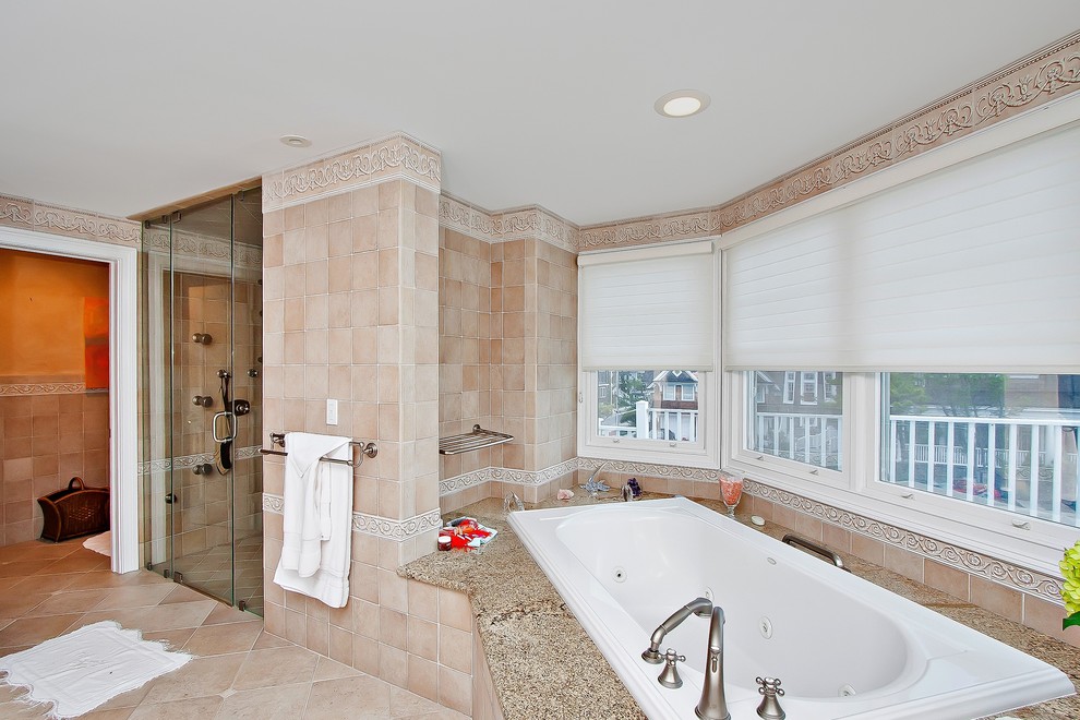 Cette image montre une très grande salle de bain principale marine avec un plan de toilette en granite, un bain bouillonnant, WC à poser et un carrelage beige.