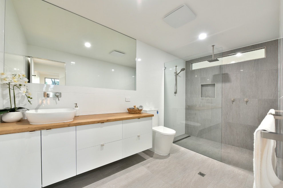 Inspiration för moderna brunt badrum med dusch, med släta luckor, vita skåp, en kantlös dusch, grå kakel, betonggolv, ett fristående handfat, träbänkskiva, grått golv, med dusch som är öppen och vita väggar
