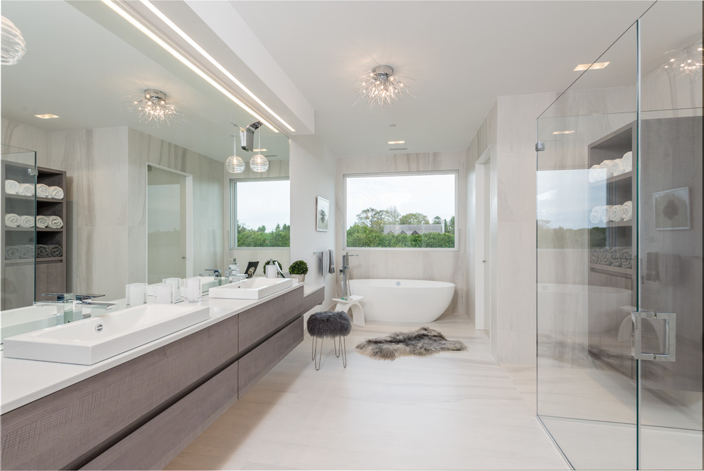 Пример оригинального дизайна: огромная главная ванная комната в современном стиле с фасадами островного типа, светлыми деревянными фасадами, отдельно стоящей ванной, душевой комнатой, инсталляцией, бежевой плиткой, керамогранитной плиткой, белыми стенами, полом из керамогранита, монолитной раковиной, белым полом и душем с распашными дверями