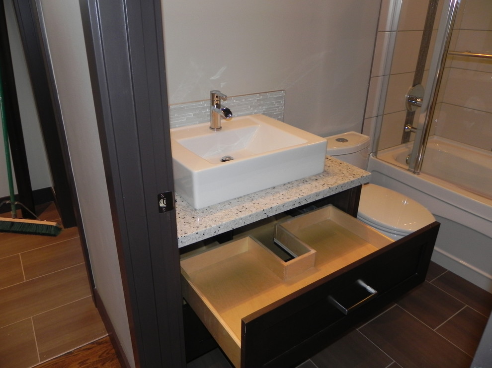 Inredning av ett klassiskt litet badrum med dusch, med släta luckor, skåp i mörkt trä, en dusch/badkar-kombination, en toalettstol med separat cisternkåpa, vit kakel, stickkakel, grå väggar, vinylgolv, ett fristående handfat, granitbänkskiva, svart golv och dusch med skjutdörr