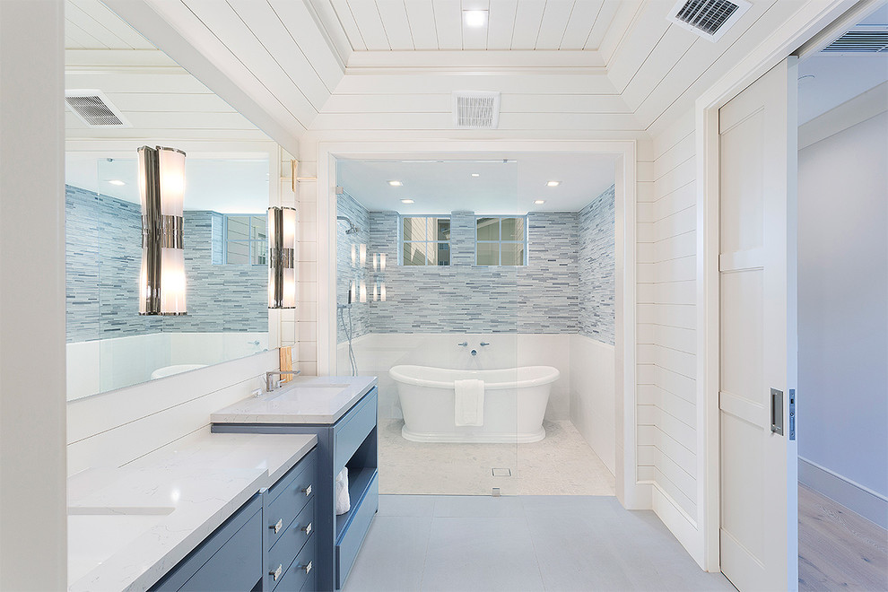 Свежая идея для дизайна: ванная комната в морском стиле с плоскими фасадами, синими фасадами, отдельно стоящей ванной, синей плиткой, удлиненной плиткой, белыми стенами, врезной раковиной, серым полом и белой столешницей - отличное фото интерьера