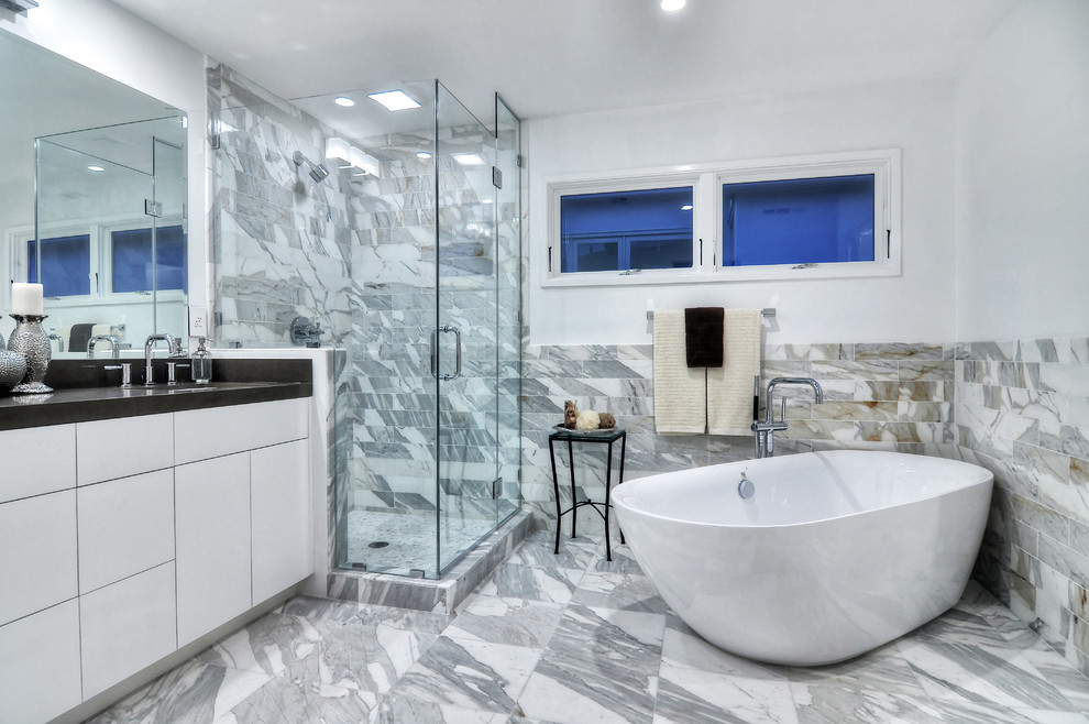 Imagen de cuarto de baño actual con armarios con paneles lisos, puertas de armario blancas, bañera exenta, ducha esquinera, baldosas y/o azulejos grises y paredes blancas