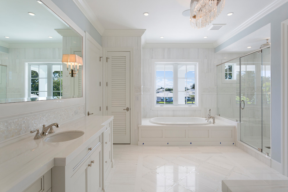 Inspiration for a tropical master white tile white floor bathroom remodel in Miami with recessed-panel cabinets, white cabinets, blue walls, an undermount sink, a hinged shower door and white countertops