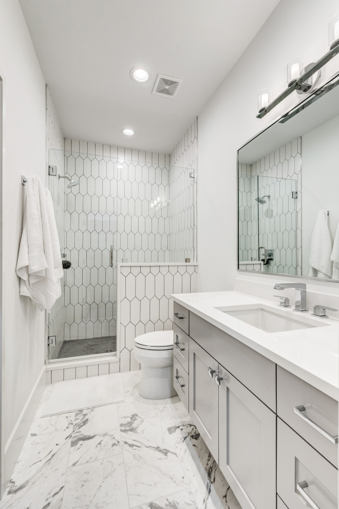 На фото: большая ванная комната в стиле неоклассика (современная классика) с фасадами в стиле шейкер, серыми фасадами, душем в нише, раздельным унитазом, белой плиткой, керамогранитной плиткой, белыми стенами, полом из керамогранита, душевой кабиной, врезной раковиной, серым полом, душем с распашными дверями, белой столешницей и встроенной тумбой с