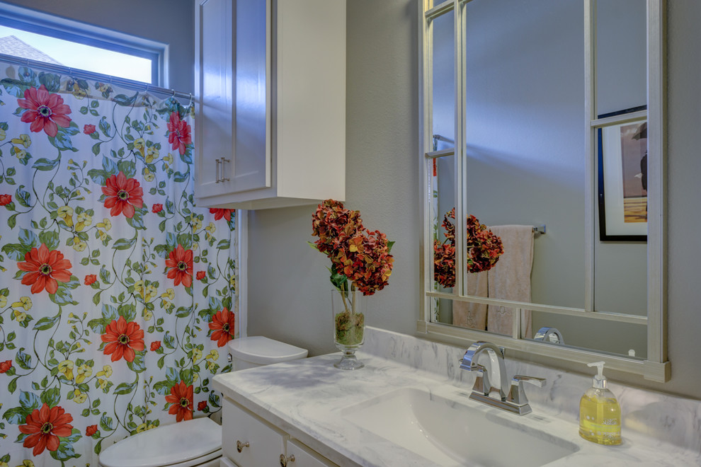 Inredning av ett klassiskt litet badrum, med skåp i shakerstil, vita skåp, ett badkar i en alkov, en dusch/badkar-kombination, en toalettstol med separat cisternkåpa, grå väggar, ett undermonterad handfat och bänkskiva i kvarts