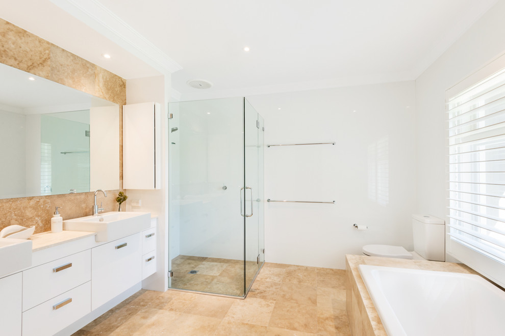 Photo of a medium sized contemporary family bathroom in Sydney with flat-panel cabinets, white cabinets, a built-in bath, a built-in shower, a one-piece toilet, white walls, travertine flooring and a built-in sink.