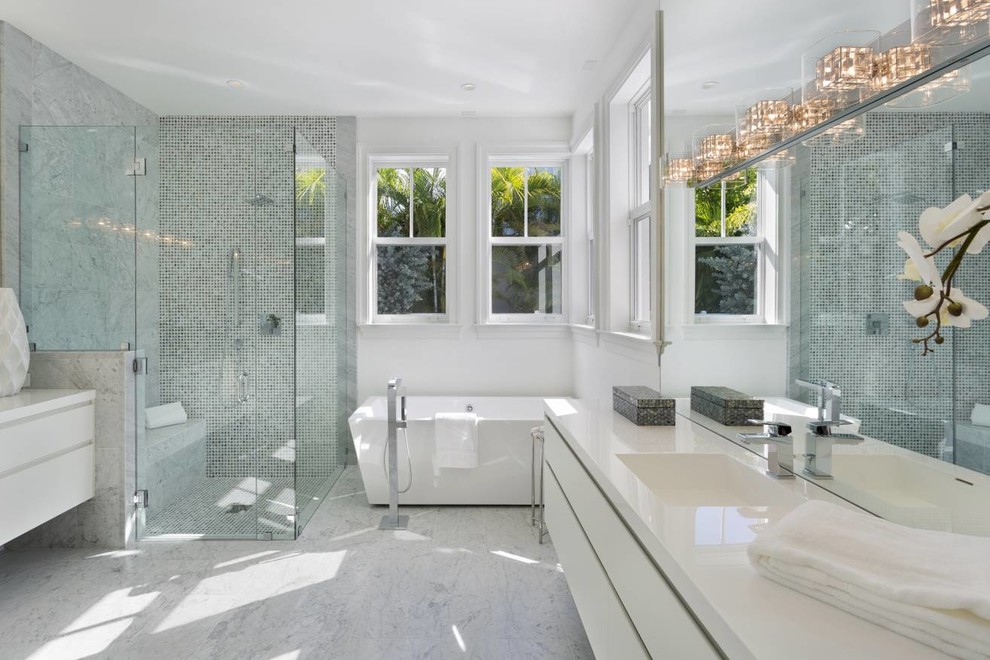 Modern inredning av ett mellanstort vit vitt en-suite badrum, med släta luckor, vita väggar, ett integrerad handfat, bänkskiva i akrylsten, vita skåp, ett fristående badkar, en hörndusch, flerfärgad kakel, mosaik, marmorgolv, dusch med gångjärnsdörr och vitt golv
