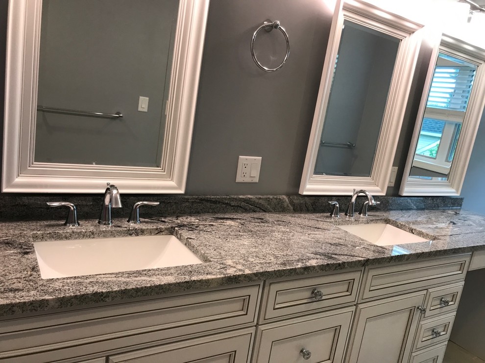 Modelo de cuarto de baño principal de tamaño medio con puertas de armario grises, encimera de granito, encimeras grises, paredes grises y lavabo bajoencimera
