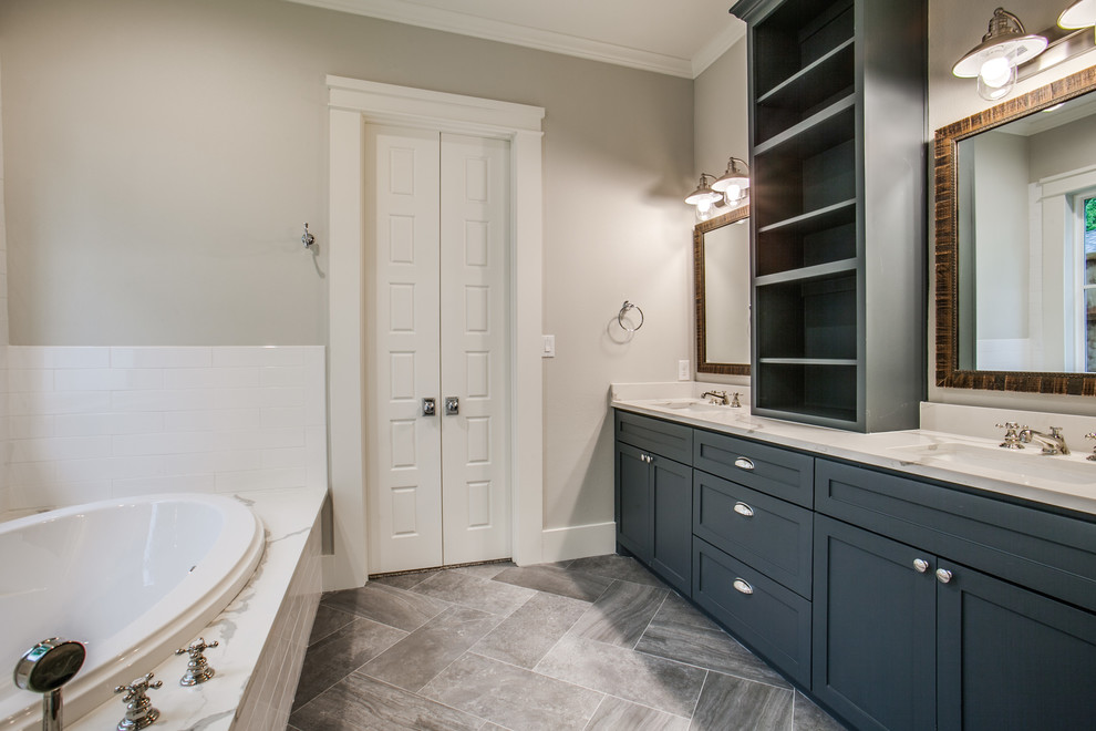 Inspiration for a mid-sized arts and crafts master bathroom in Dallas with shaker cabinets, blue cabinets, a drop-in tub, a corner shower, a two-piece toilet, gray tile, porcelain tile, grey walls, porcelain floors, an undermount sink and engineered quartz benchtops.
