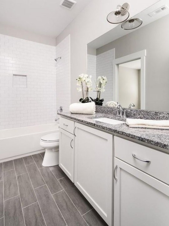 Mid-sized elegant 3/4 white tile and ceramic tile laminate floor and black floor bathroom photo in Atlanta with raised-panel cabinets, white cabinets, an undermount tub, a one-piece toilet, white walls, an undermount sink, marble countertops and black countertops