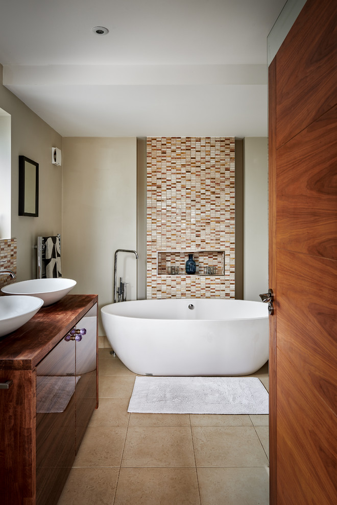 На фото: ванная комната в современном стиле с плоскими фасадами, фасадами цвета дерева среднего тона, отдельно стоящей ванной, бежевыми стенами, настольной раковиной, столешницей из дерева, бежевым полом и коричневой столешницей с