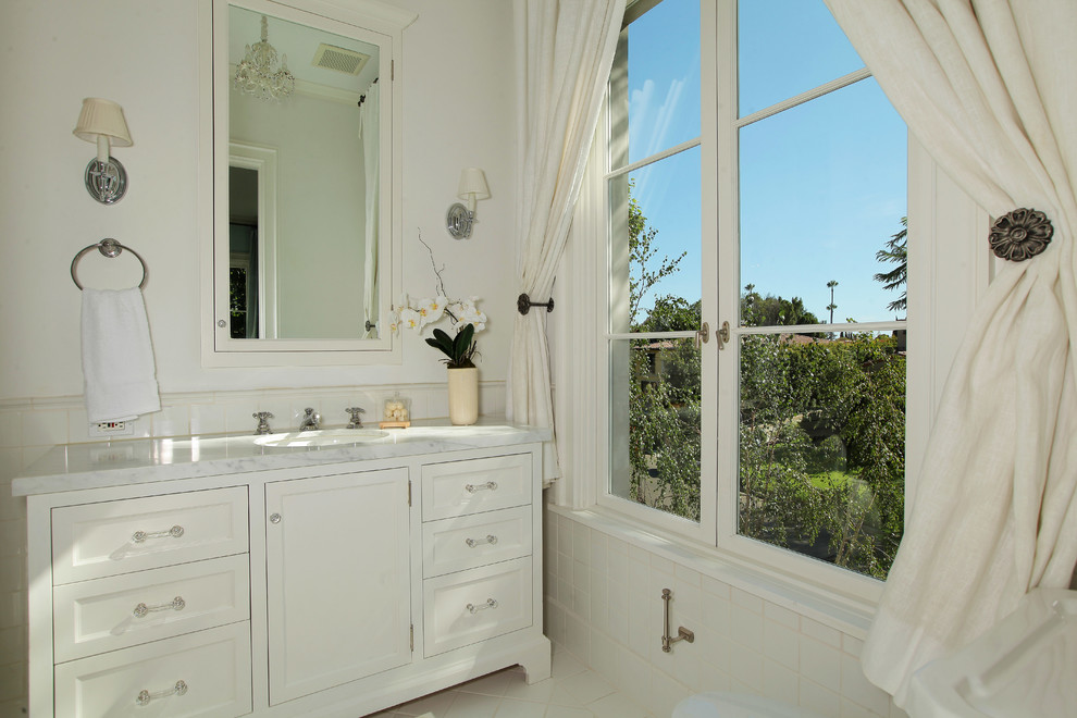 Modelo de cuarto de baño tradicional con lavabo bajoencimera, armarios con paneles empotrados, puertas de armario blancas y baldosas y/o azulejos blancos