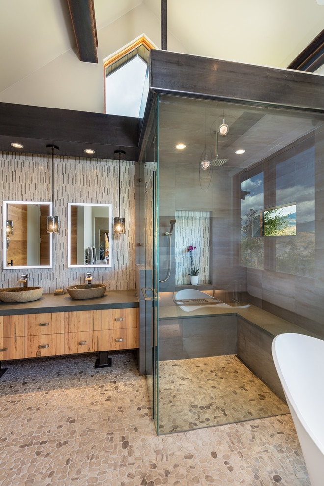 Cette image montre une salle de bain chalet en bois brun avec un placard à porte plane, une baignoire indépendante, une douche d'angle, un sol en galet, une vasque, un sol beige, une cabine de douche à porte battante et un plan de toilette gris.
