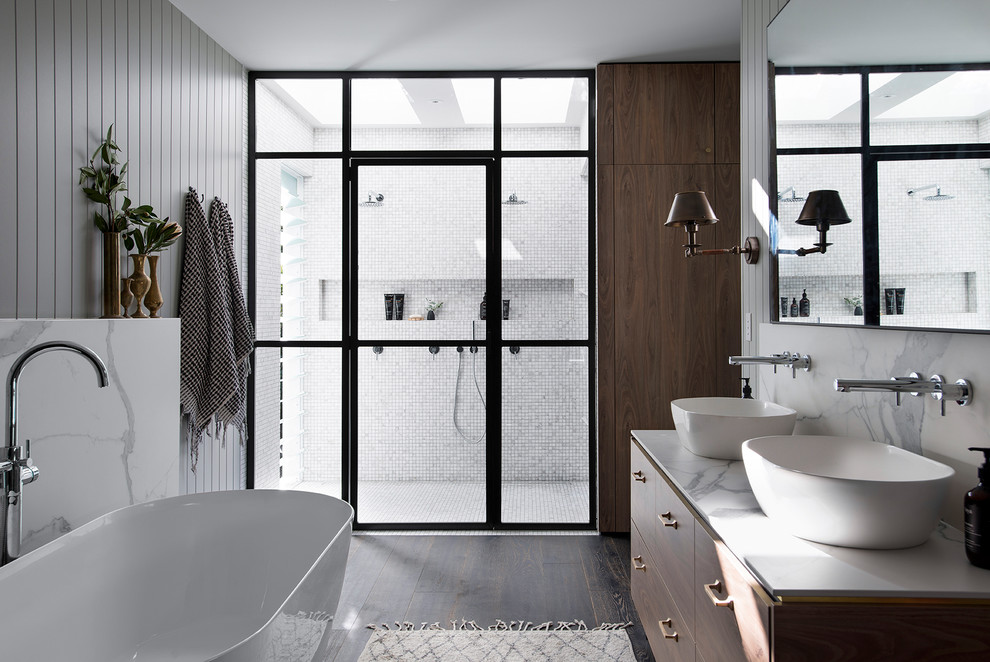 Aménagement d'une salle de bain moderne en bois brun avec une baignoire indépendante, une douche double, un carrelage blanc, des carreaux de porcelaine, parquet foncé, un sol marron, une cabine de douche à porte battante et un plan de toilette blanc.
