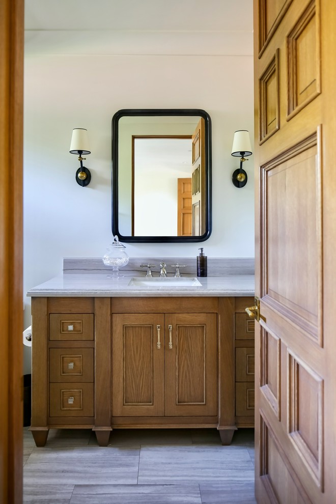 Cette photo montre une salle de bain craftsman en bois brun avec un placard avec porte à panneau encastré, un mur blanc, un sol en carrelage de porcelaine, un lavabo encastré, un plan de toilette en marbre, un sol gris et un plan de toilette gris.