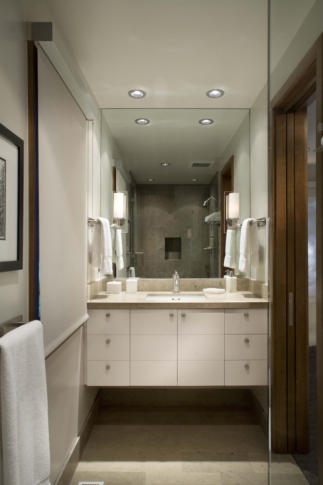 Ejemplo de cuarto de baño actual con lavabo bajoencimera, armarios con paneles lisos, puertas de armario blancas y baldosas y/o azulejos beige