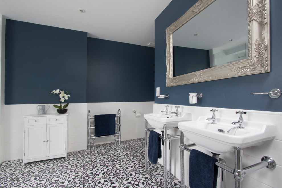 Klassisches Badezimmer mit weißen Fliesen, blauer Wandfarbe, Waschtischkonsole, buntem Boden und Doppelwaschbecken in Sonstige