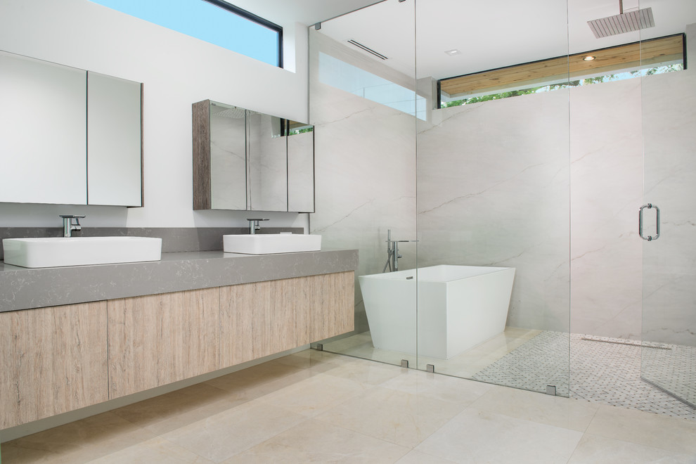 Aménagement d'une salle de bain principale contemporaine en bois clair avec un placard à porte plane, une baignoire indépendante, un espace douche bain, un carrelage blanc, un mur blanc, une vasque, un sol beige, une cabine de douche à porte battante et un plan de toilette gris.