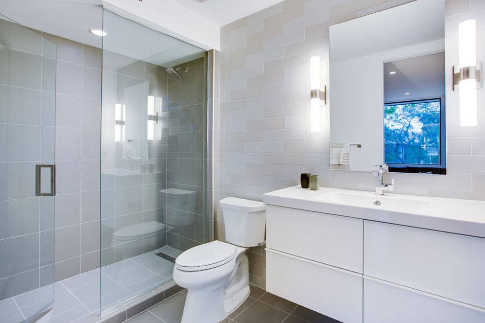 Inredning av ett modernt mellanstort badrum, med ett integrerad handfat, släta luckor, vita skåp, bänkskiva i kvarts, en öppen dusch, en toalettstol med separat cisternkåpa, grå kakel, porslinskakel, vita väggar och klinkergolv i porslin