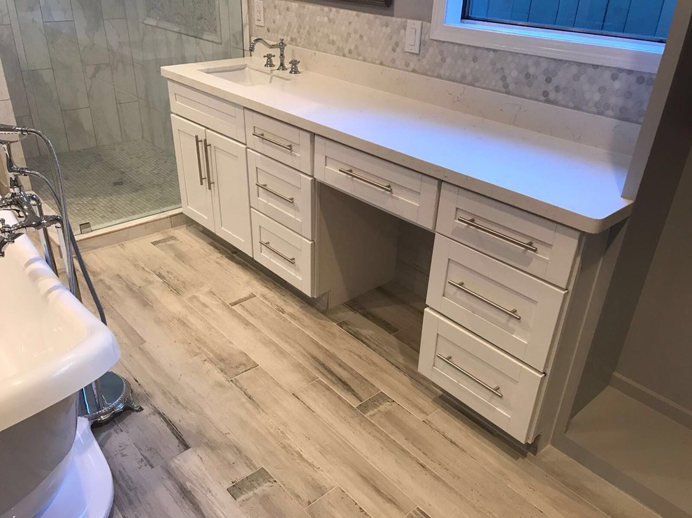 Medium sized traditional ensuite bathroom in Houston with shaker cabinets, white cabinets, a freestanding bath, a corner shower, white tiles, stone tiles, grey walls, vinyl flooring, a submerged sink, quartz worktops, grey floors and a hinged door.