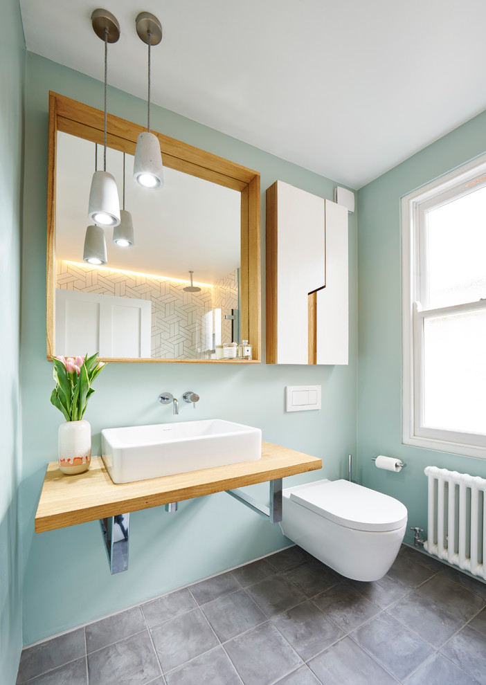 This is an example of a medium sized contemporary bathroom in London with flat-panel cabinets, white cabinets, a wall mounted toilet, green walls, a vessel sink, wooden worktops and grey floors.