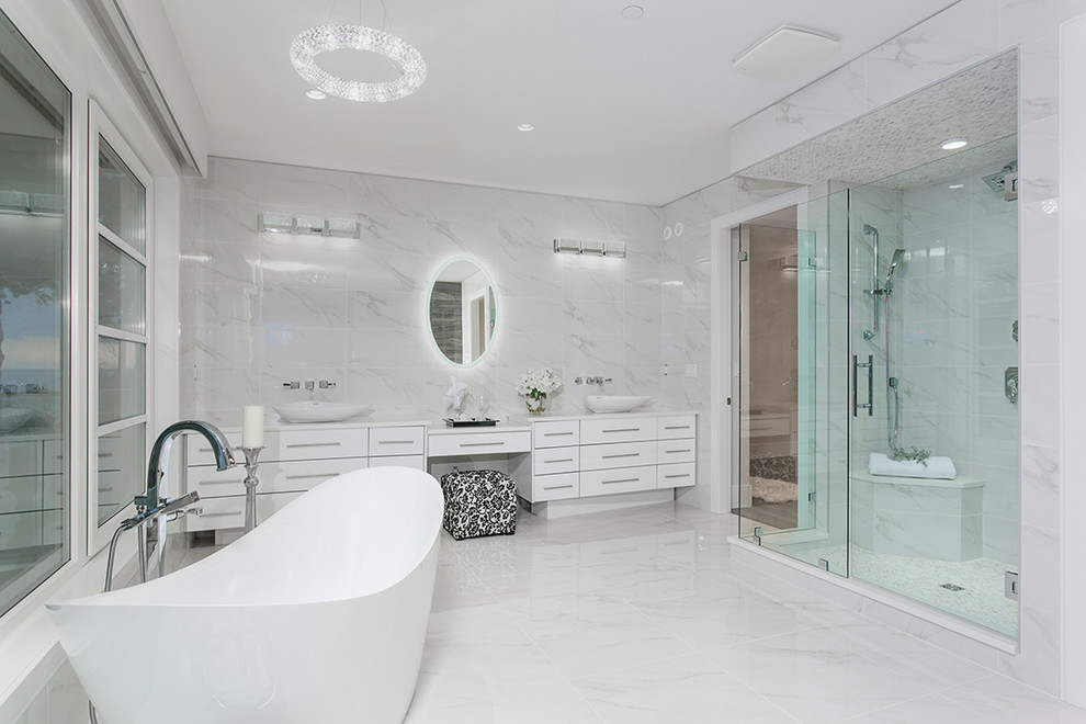 Пример оригинального дизайна: большая главная ванная комната в современном стиле с плоскими фасадами, белыми фасадами, отдельно стоящей ванной, душем в нише, раздельным унитазом, белой плиткой, керамогранитной плиткой, белыми стенами, полом из керамогранита, настольной раковиной, столешницей из искусственного кварца, белым полом, душем с распашными дверями и белой столешницей