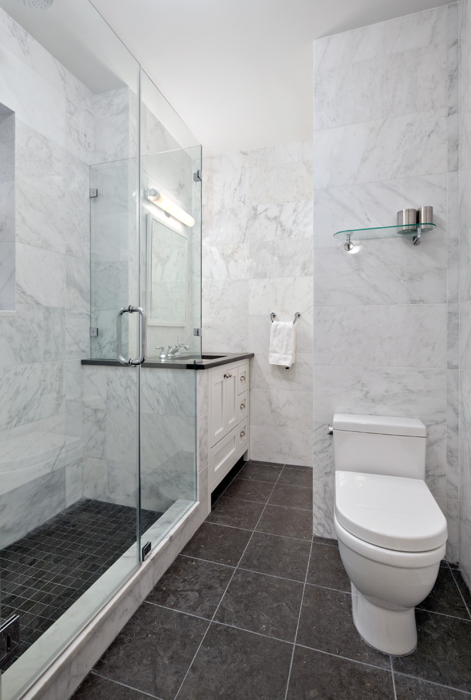 Corner shower - small transitional 3/4 black tile and glass tile porcelain tile corner shower idea in New York with shaker cabinets, white cabinets, a one-piece toilet, white walls and granite countertops