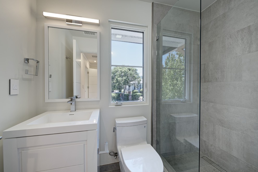 Bathroom - mid-sized transitional 3/4 gray tile and cement tile porcelain tile and gray floor bathroom idea in San Francisco with flat-panel cabinets, white cabinets, a one-piece toilet, gray walls, an integrated sink, quartz countertops and a hinged shower door