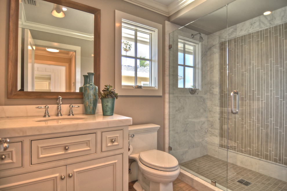 Immagine di una stanza da bagno costiera con lavabo sottopiano, ante a filo, ante bianche, doccia alcova e piastrelle grigie
