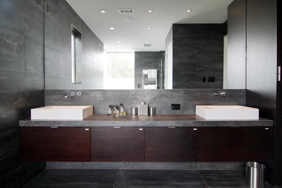 Foto de cuarto de baño rectangular contemporáneo con encimera de cemento, armarios con paneles lisos, puertas de armario de madera en tonos medios, baldosas y/o azulejos grises, paredes grises, lavabo sobreencimera y suelo gris