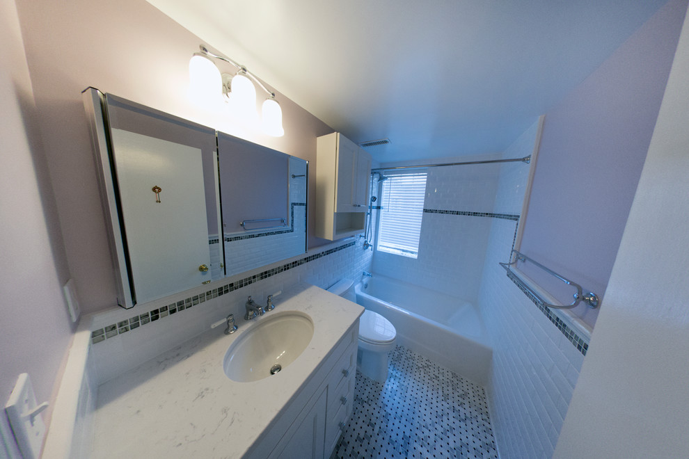 ワシントンD.C.にある中くらいなトランジショナルスタイルのおしゃれな浴室 (アンダーカウンター洗面器、シェーカースタイル扉のキャビネット、白いキャビネット、クオーツストーンの洗面台、アルコーブ型浴槽、シャワー付き浴槽	、一体型トイレ	、白いタイル、サブウェイタイル、紫の壁、大理石の床) の写真