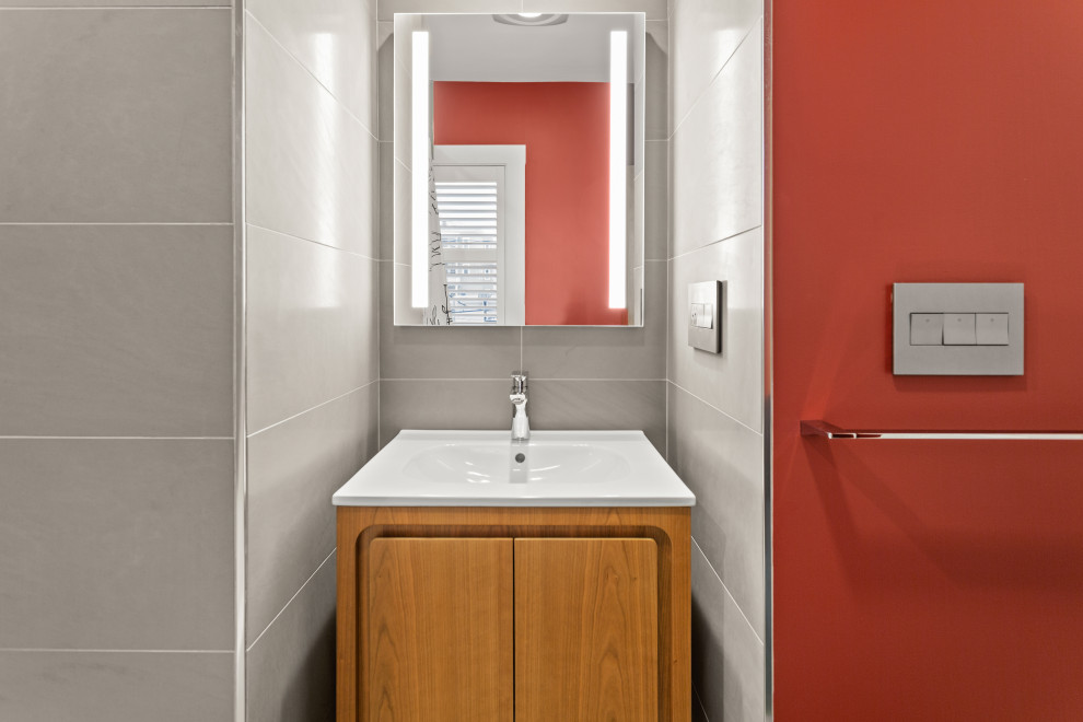 Cette photo montre une salle de bain moderne en bois clair de taille moyenne avec un placard à porte plane, une baignoire en alcôve, un combiné douche/baignoire, un carrelage gris, des carreaux de porcelaine, un mur gris, un lavabo intégré, un plan de toilette en surface solide, une cabine de douche avec un rideau et un plan de toilette blanc.