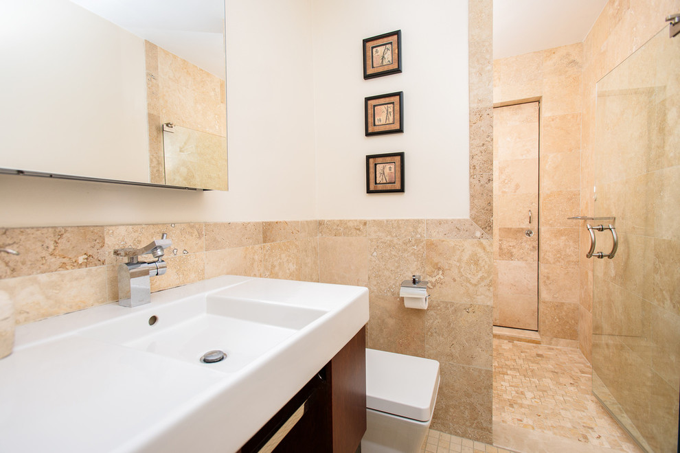 Example of a large minimalist master beige tile and limestone tile ceramic tile doorless shower design in Boston with flat-panel cabinets, brown cabinets, a one-piece toilet, white walls, an integrated sink and solid surface countertops