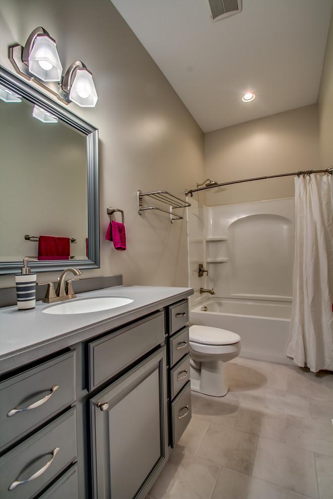 Diseño de cuarto de baño tradicional con lavabo integrado, armarios con paneles con relieve, puertas de armario grises, encimera de acrílico, combinación de ducha y bañera, baldosas y/o azulejos grises y paredes grises
