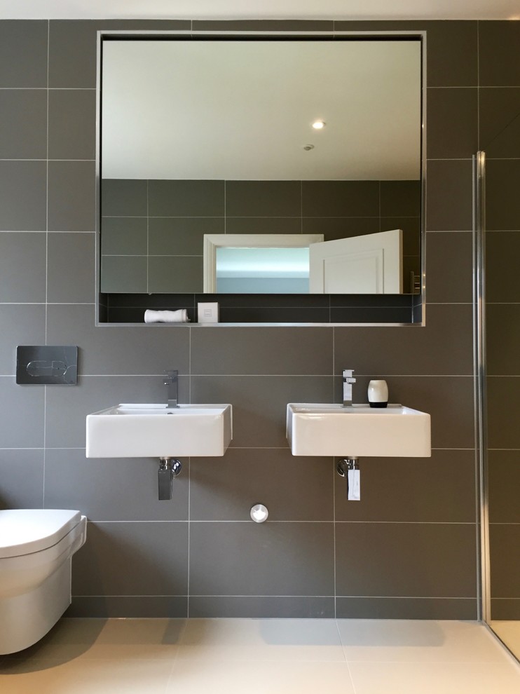 Foto på ett funkis badrum, med ett väggmonterat handfat, en kantlös dusch, en vägghängd toalettstol, grå kakel och grå väggar