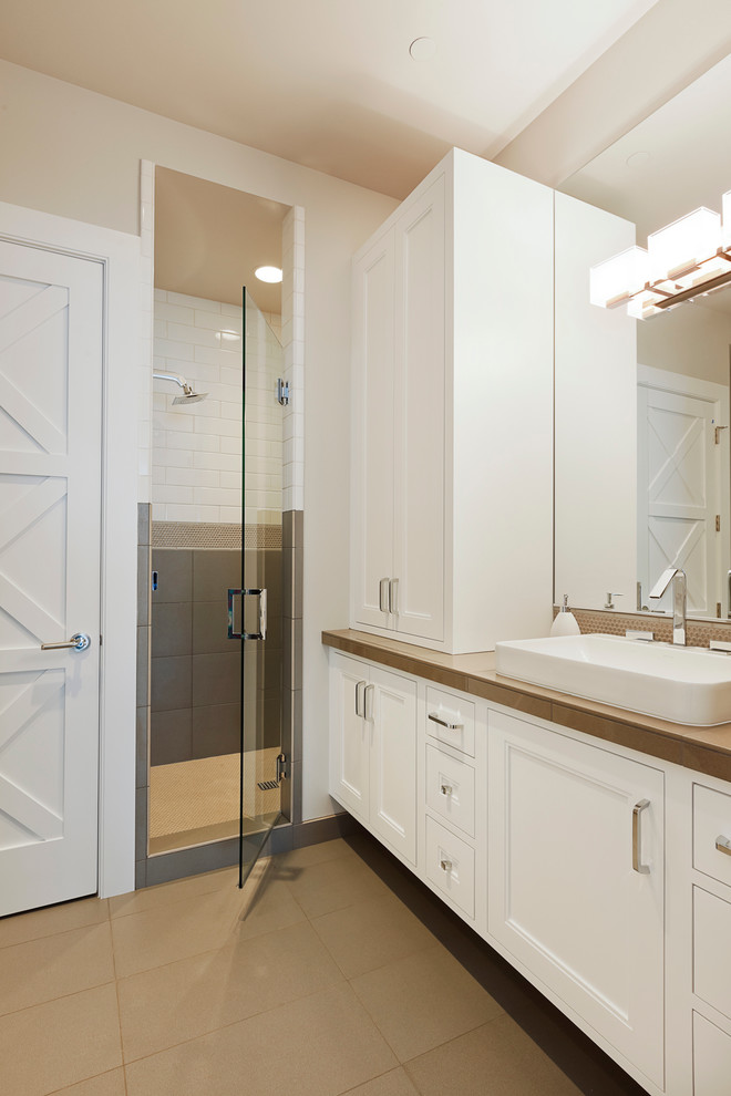 На фото: ванная комната в современном стиле с настольной раковиной, фасадами с утопленной филенкой, белыми фасадами, душем в нише, белой плиткой, плиткой кабанчик и коричневой столешницей