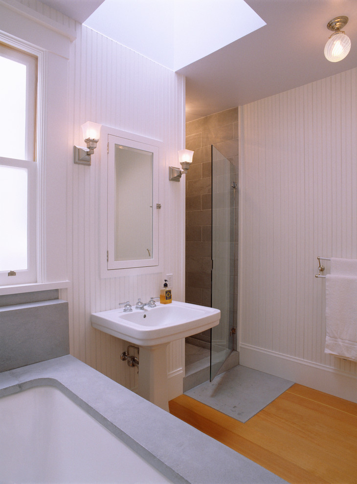Inredning av ett klassiskt mellanstort badrum, med ett piedestal handfat, ett undermonterat badkar, cementkakel, vita väggar och ljust trägolv