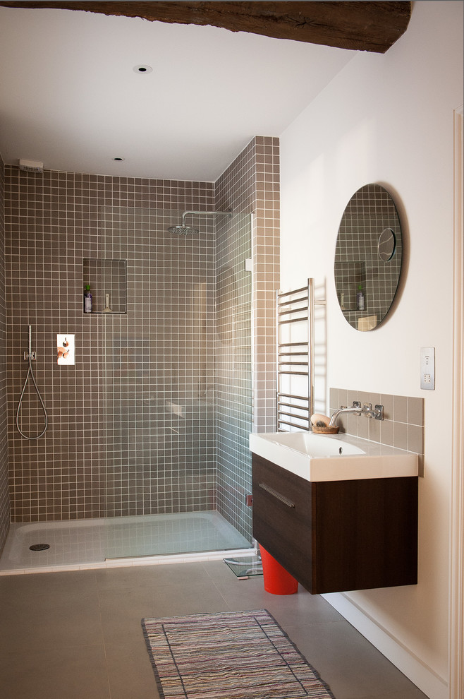 This is an example of a medium sized contemporary shower room bathroom in Oxfordshire with a wall-mounted sink, flat-panel cabinets, dark wood cabinets, solid surface worktops, brown tiles, ceramic tiles, white walls, porcelain flooring, a walk-in shower, an open shower and beige floors.