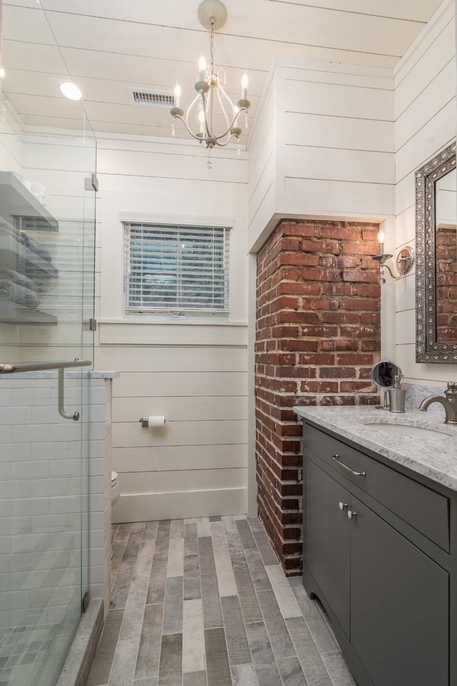 Bild på ett mellanstort lantligt badrum med dusch, med släta luckor, grå skåp, en hörndusch, vit kakel, tunnelbanekakel, vita väggar, klinkergolv i porslin, ett undermonterad handfat och marmorbänkskiva