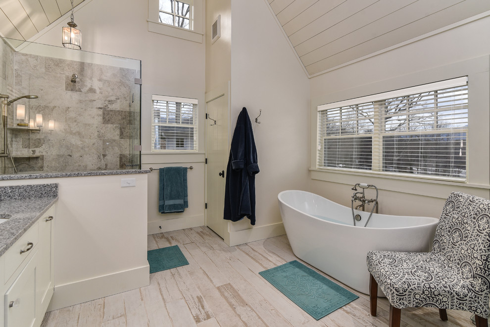 Photo of a large country ensuite bathroom in Other with recessed-panel cabinets, white cabinets, a freestanding bath, a corner shower, stone tiles, white walls, light hardwood flooring, a submerged sink and granite worktops.