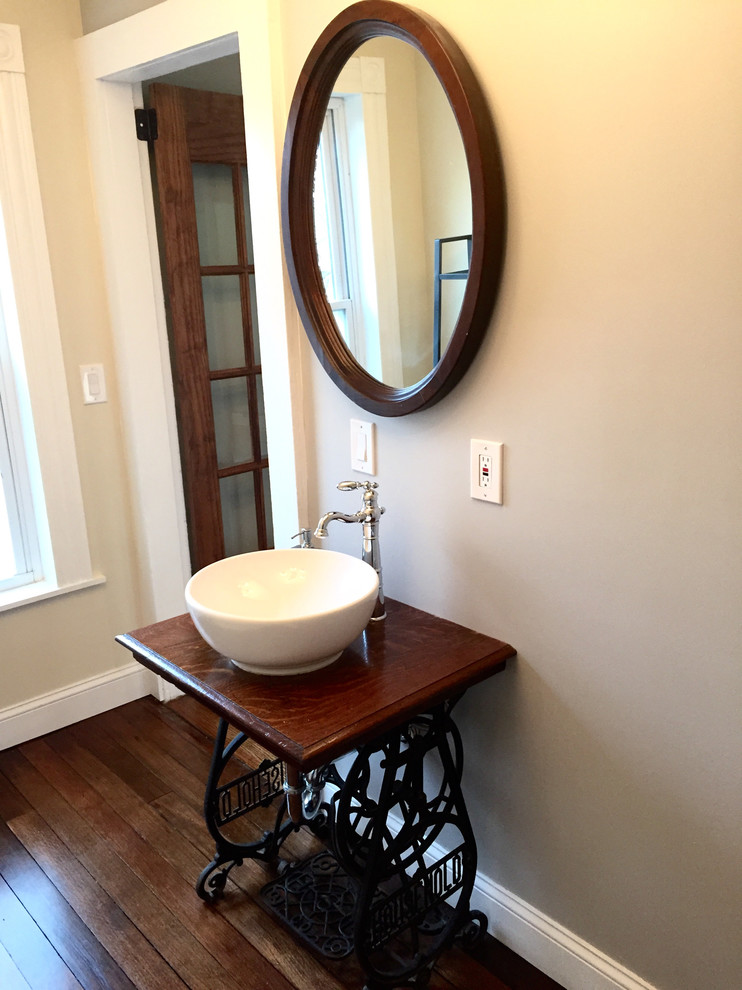 Cette image montre une salle d'eau victorienne en bois brun de taille moyenne avec un placard en trompe-l'oeil, un mur gris, un sol en bois brun, une vasque et un plan de toilette en bois.