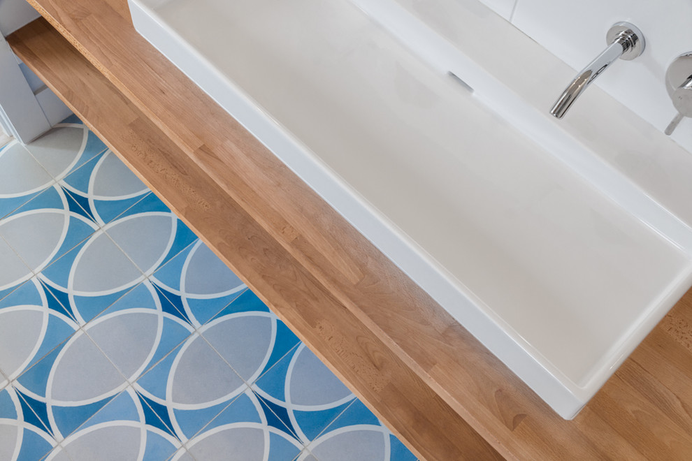 Exemple d'une salle de bain moderne en bois clair avec un carrelage bleu, des carreaux de béton, un mur blanc, sol en béton ciré, une vasque et un plan de toilette en bois.