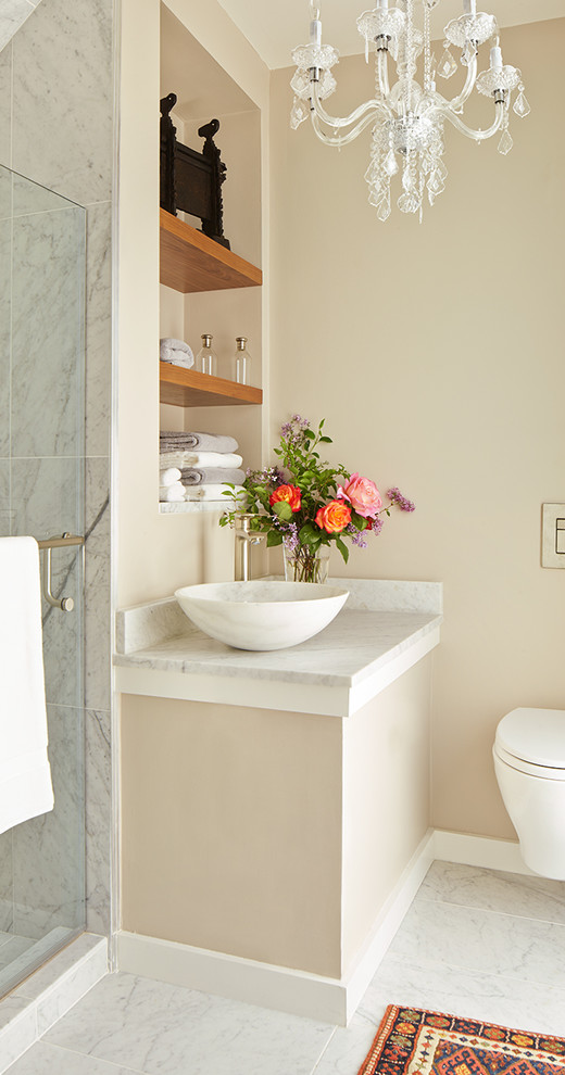 Cette image montre une petite salle de bain traditionnelle avec une vasque, un placard sans porte, des portes de placard blanches, un plan de toilette en marbre, WC suspendus, un carrelage de pierre, un mur beige et un sol en marbre.
